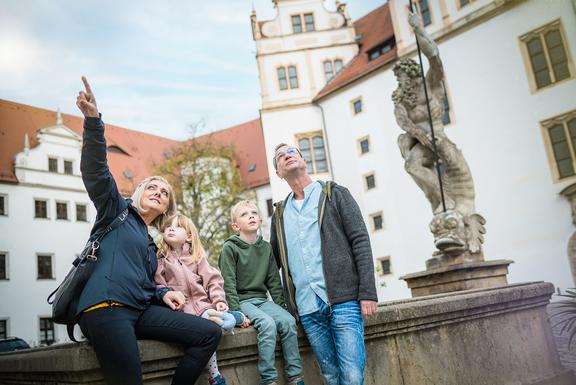 Eine Familie sitzt auf dem Brunnen im Schlosshof und sieht sich um