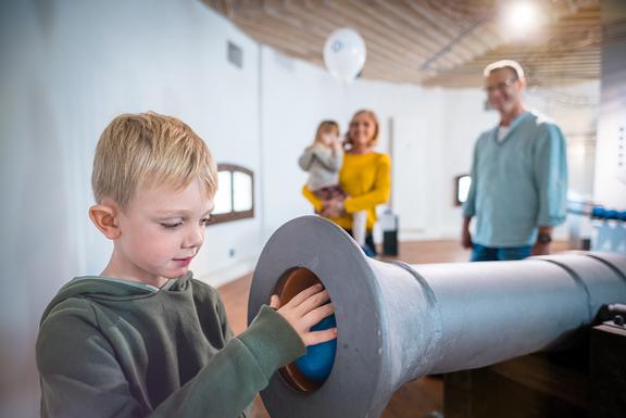 Ein Junge steckt eine Kanonenkugel in das Kanonenrohr in der Ausstellung STANDFEST. BIBELFEST. TRINKFEST.