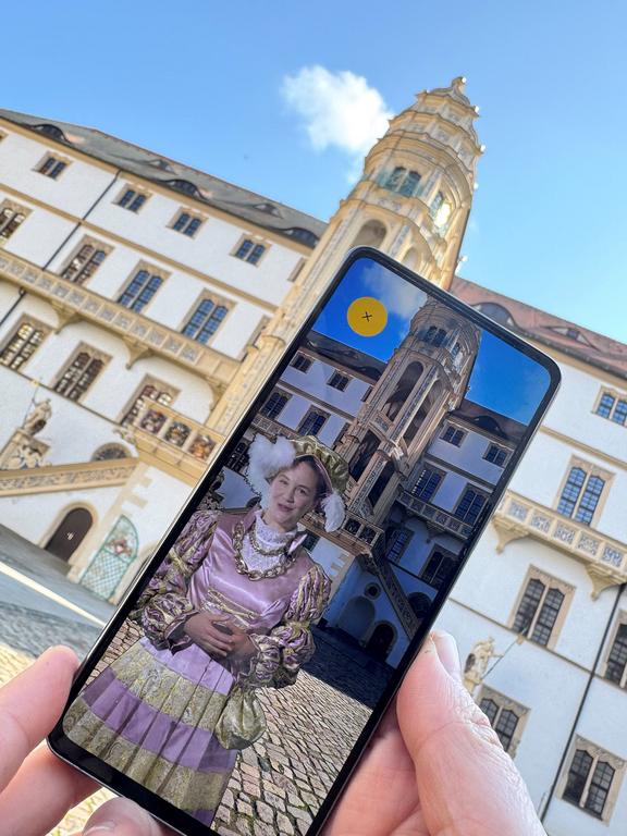 Smartphone wird vor den Großen Wendelstein gehalten. Auf dem Screen ist Kurfürstin Sibylle als Avatar zu sehen.