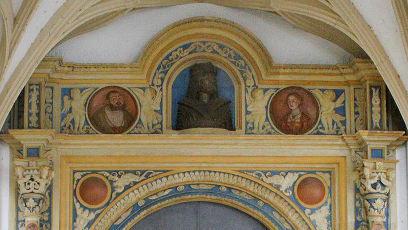 Blick auf das Portal. Oberhalb der Tür thront eine Büste Friedrich des Weisen, rechts und links davon sind Medaillons von Kurfürst Johann Friedrich und seiner Frau Sybille angebracht. Rechts und links von der Tür strecken sich zwei Säulen empor, an denen kleinere Medaillons von Martin Luther und Philipp Melanchton befestigt sind.